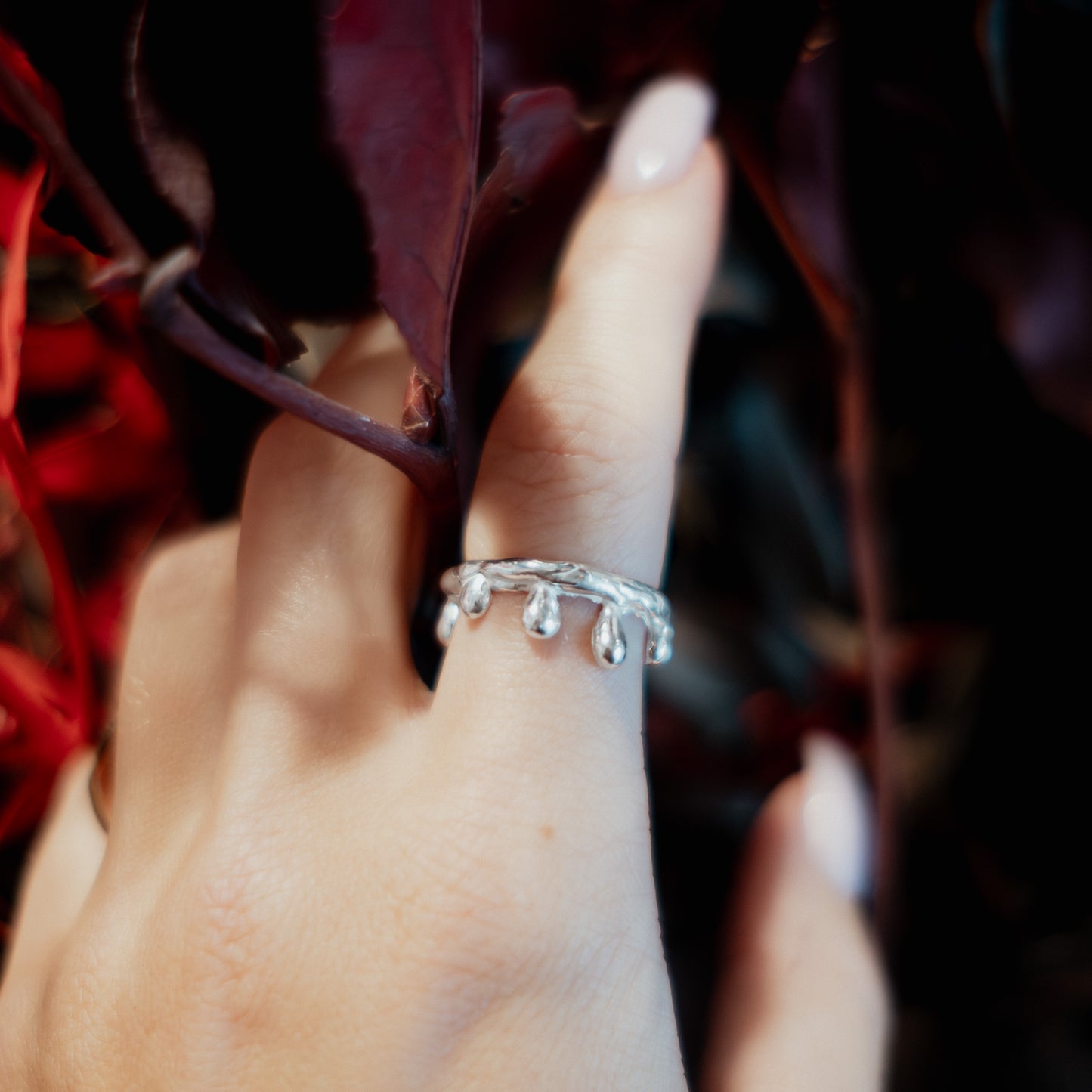Hand wearing a silver ring with a blurred red leaf background