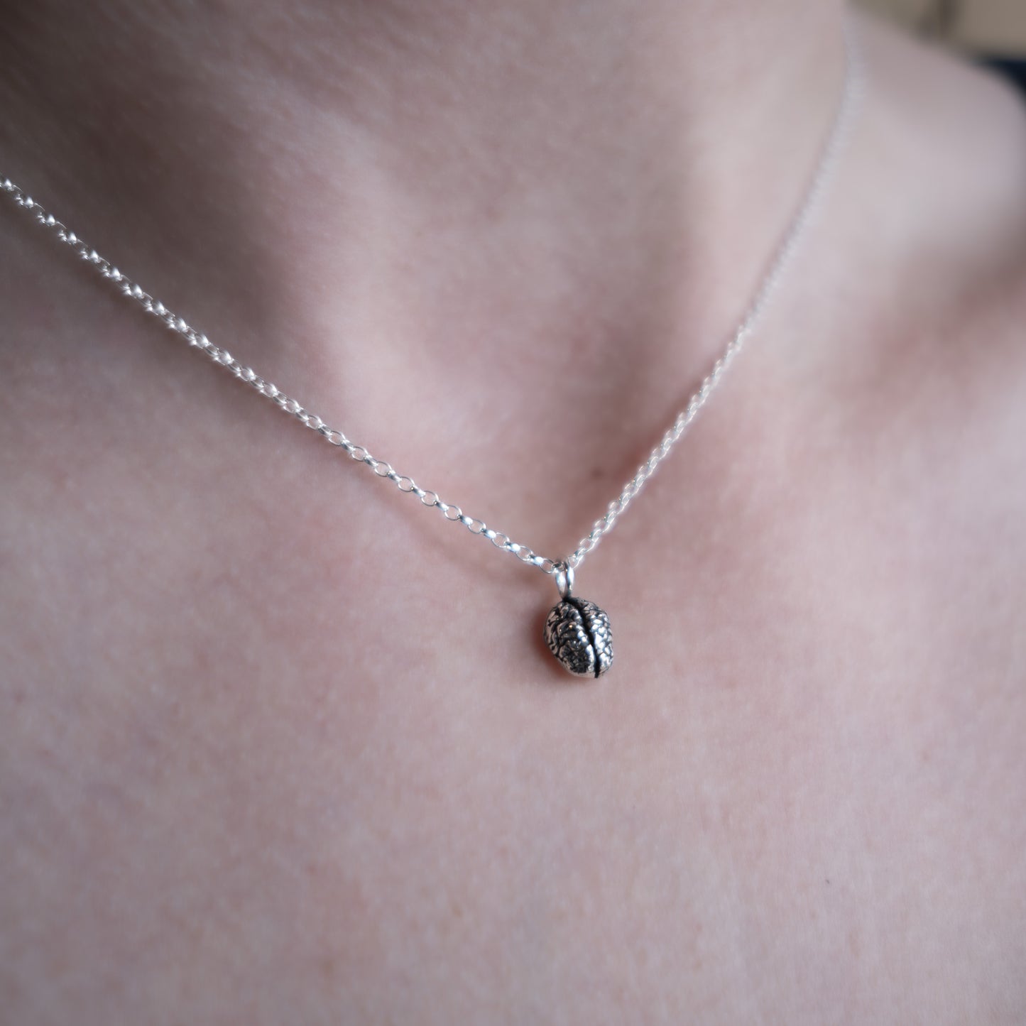 Silver necklace with a small pendant on a person's neck against a neutral background