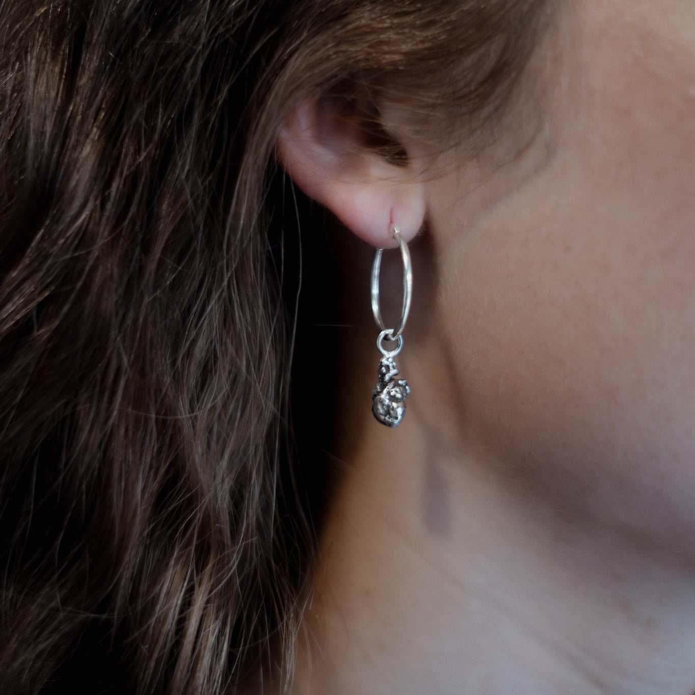 Close-up of a person wearing a silver hoop earring with a small dangling heart charm.