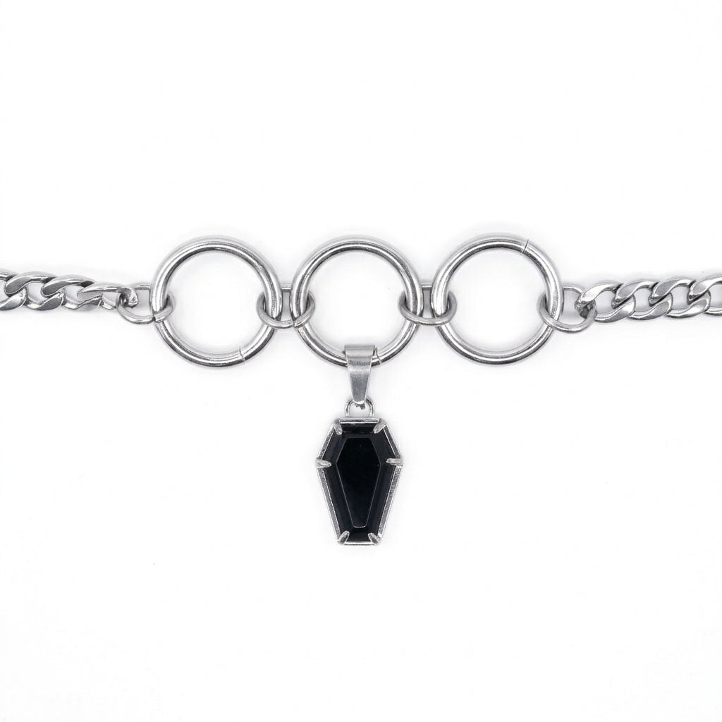 A silver-toned chain bracelet featuring three large interlocking circular rings and a dangling coffin-shaped black gemstone pendant, shown on a plain white background.