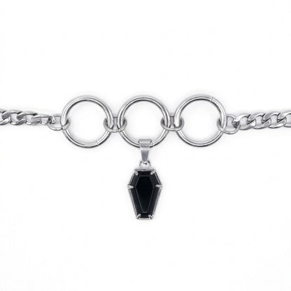 A silver-toned chain bracelet featuring three large interlocking circular rings and a dangling coffin-shaped black gemstone pendant, shown on a plain white background.