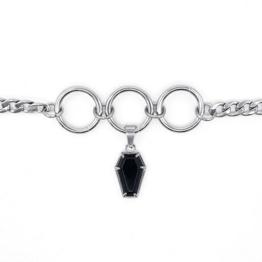 A silver-toned chain bracelet featuring three large interlocking circular rings and a dangling coffin-shaped black gemstone pendant, shown on a plain white background.