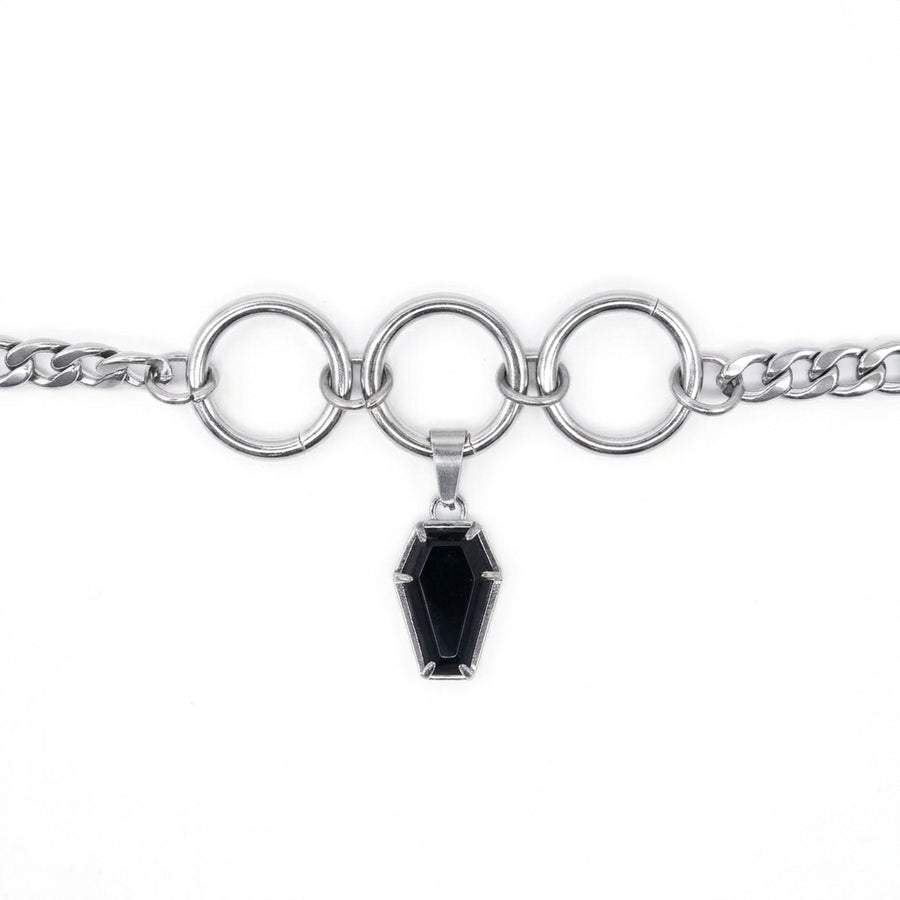 A silver-toned chain bracelet featuring three large interlocking circular rings and a dangling coffin-shaped black gemstone pendant, shown on a plain white background.