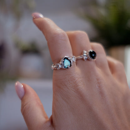 Close-up of a hand wearing two rings with gemstones against a blurred background