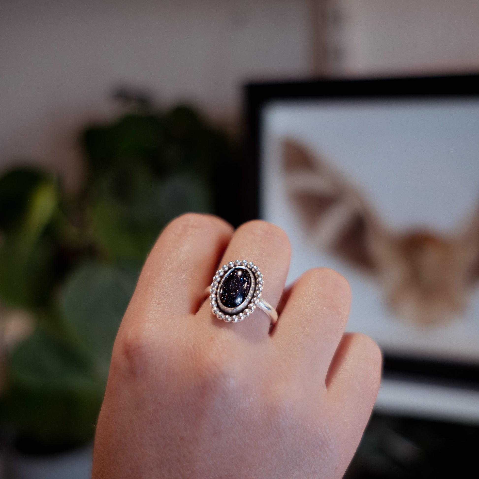 Hand wearing a silver ring with a dark gemstone, blurred background