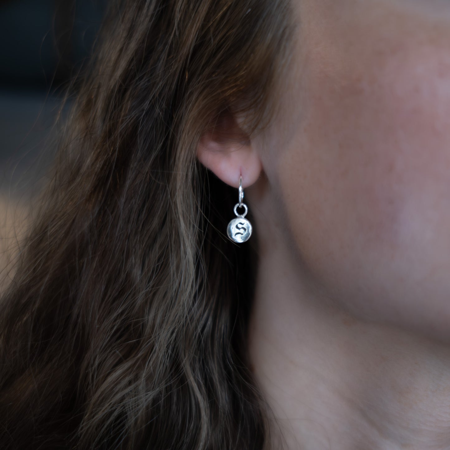 Close-up of an ear wearing a silver earring with a circular charm.