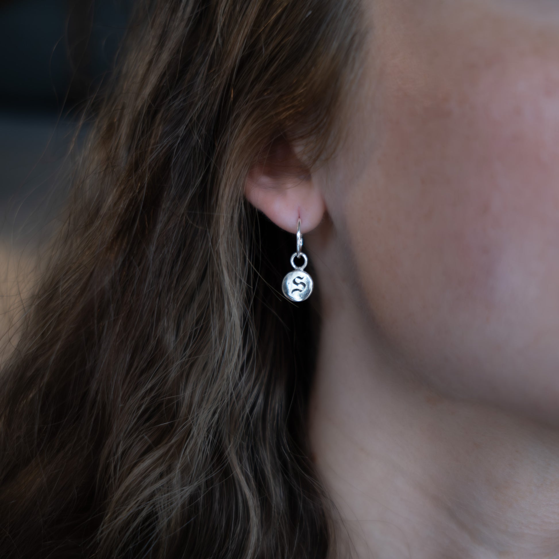 Close-up of an ear wearing a silver earring with a circular charm.