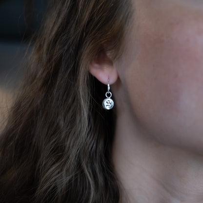 Close-up of an ear wearing a silver earring with a circular charm.