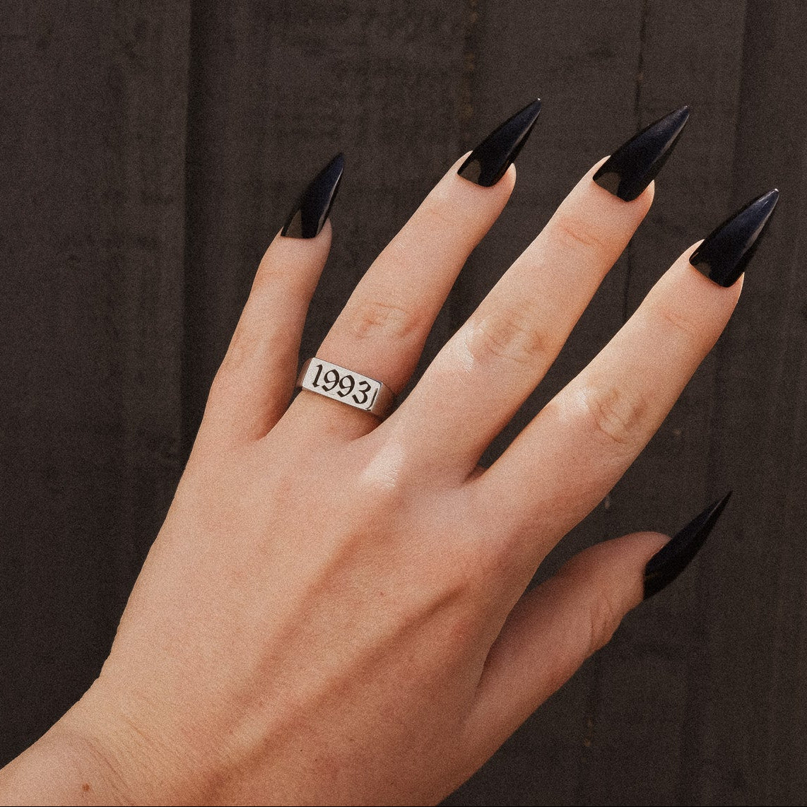 Hand with black nail polish and a ring on a dark background