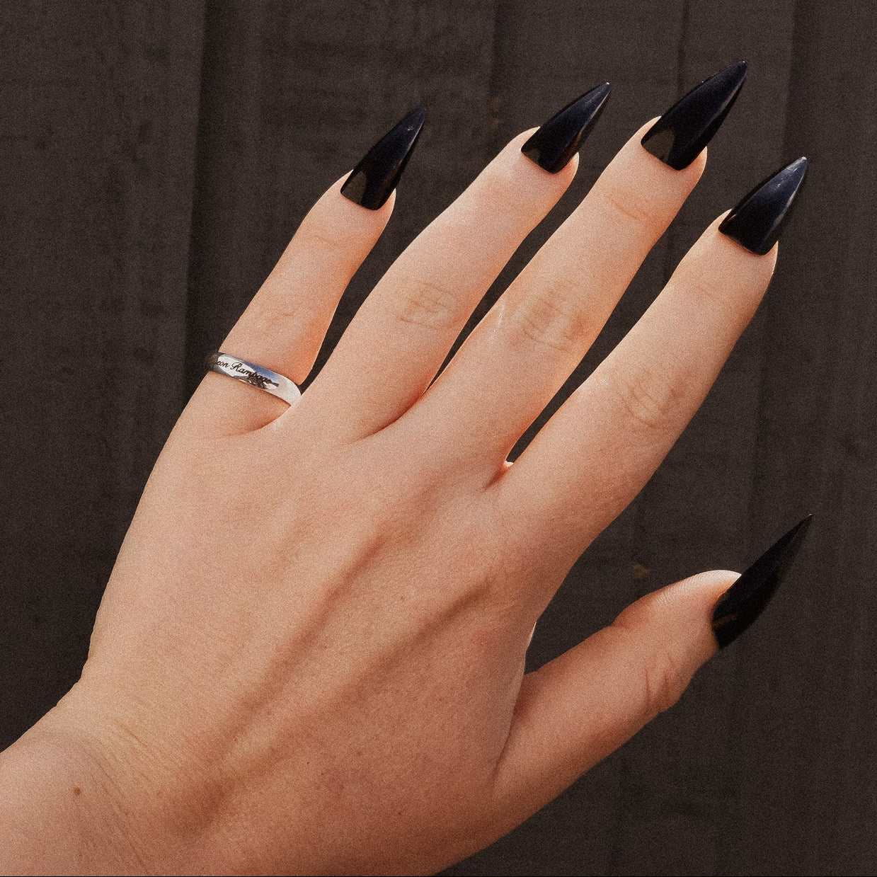 Hand with black nail polish wearing a silver ring against a dark background