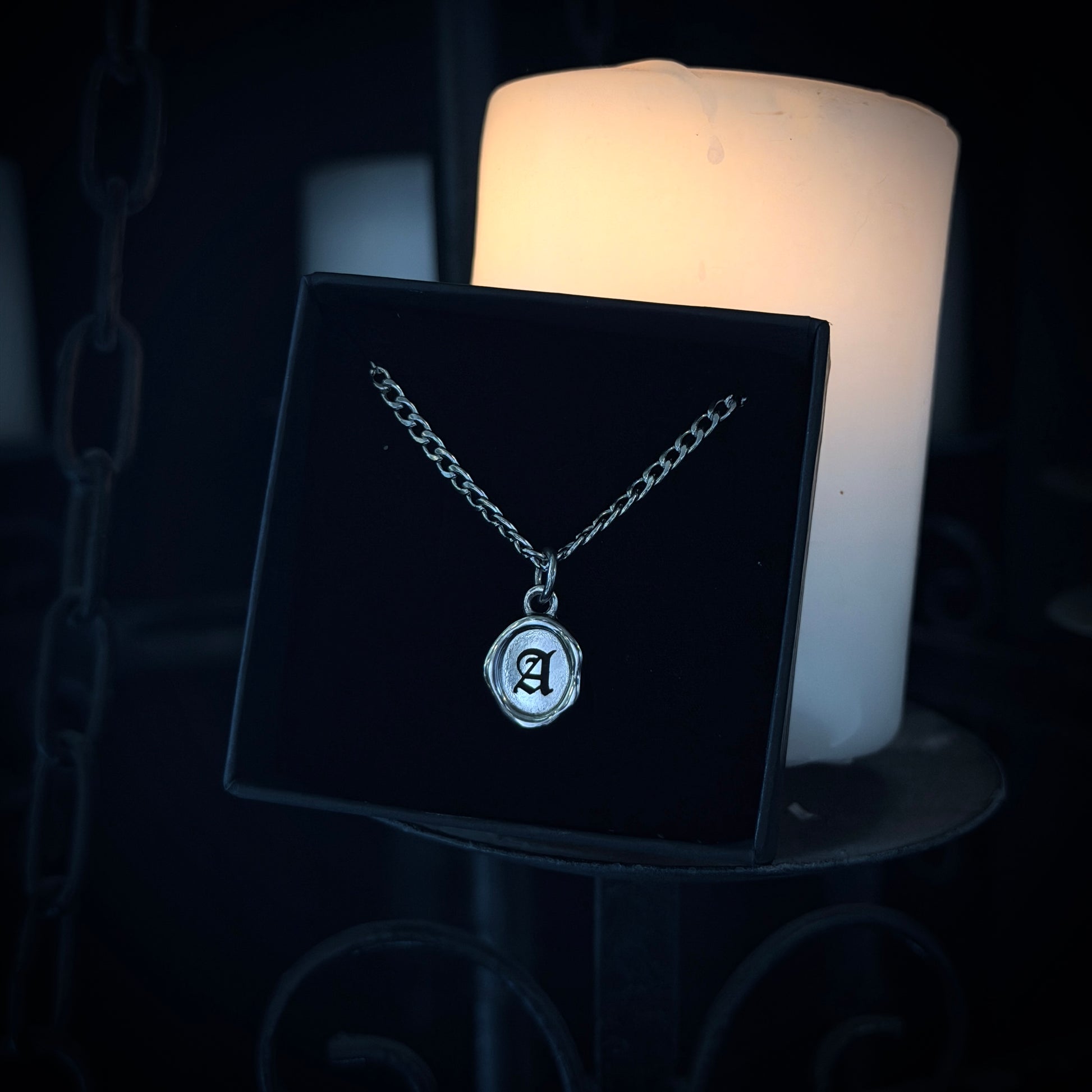 Silver necklace with a pendant on a black stand in front of a candle