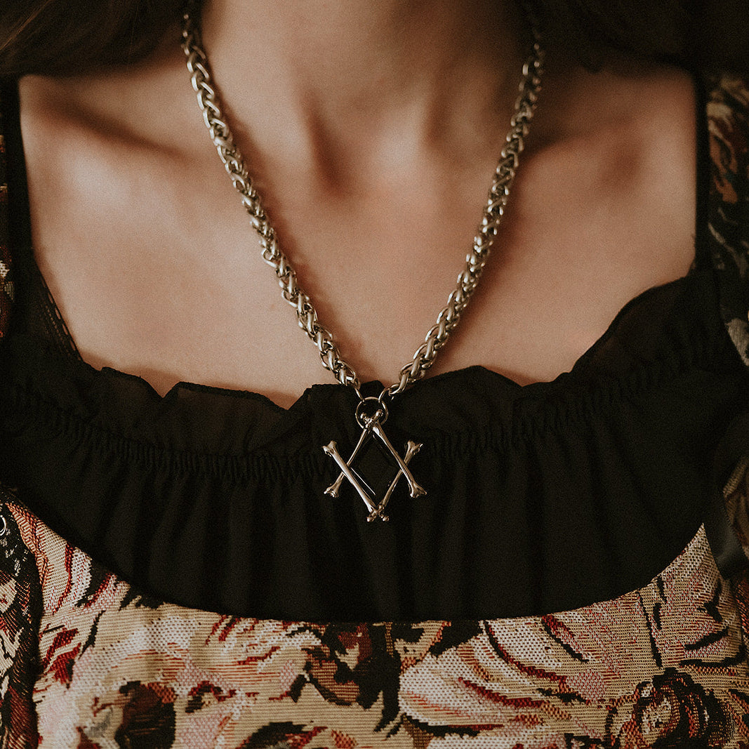 Necklace with a bone pendant worn by a person in a patterned top.