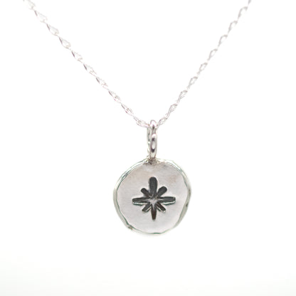 Silver necklace with a round pendant featuring a star design on a white background