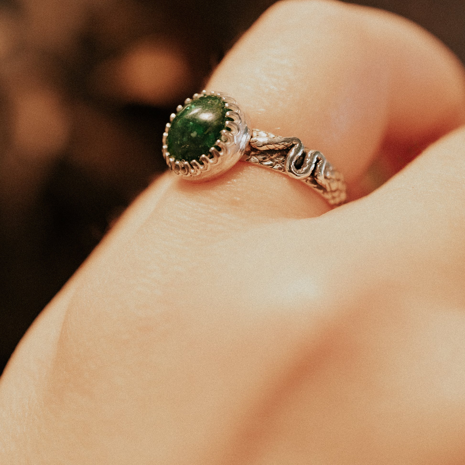 Silver ring with a green gemstone on a finger against a blurred background